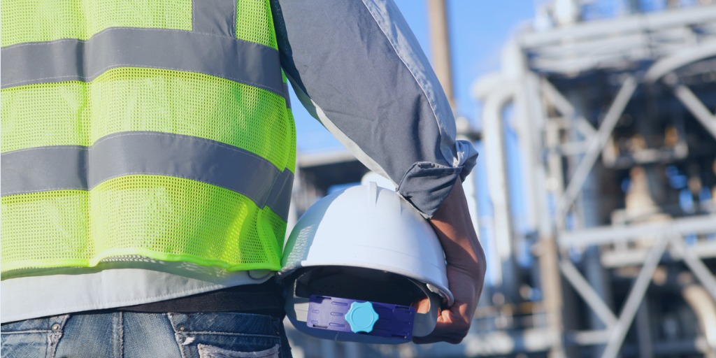 Promoting a sustainable process safety culture. Engineer holding a hard hat with a refinery in the background